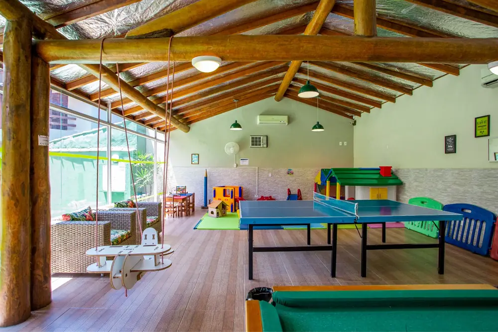 Salão de jogos coberto com mesa de pingue-pongue, sinuca, balanço em forma de avião e casinha de brinquedo