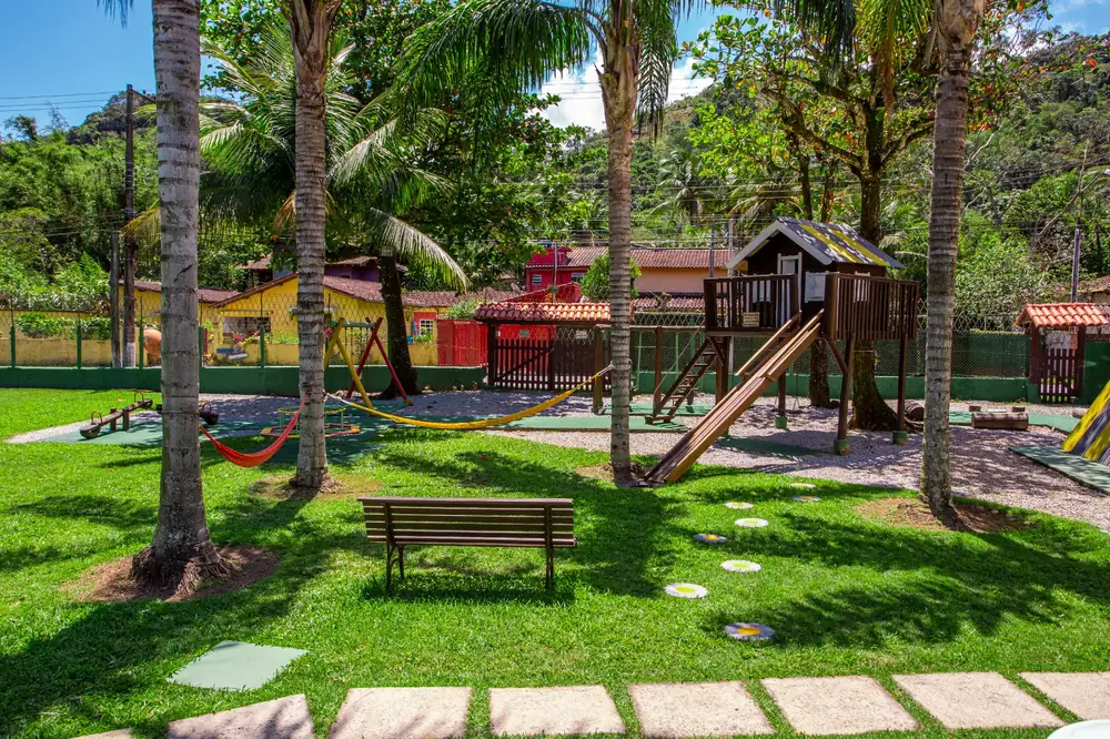 Parquinho no jardim com casa na árvore, escorregador, redes e gangorra entre coqueiros